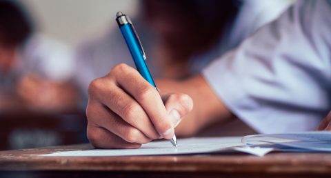 Close-up to student holding pen and writing final exam in examination room or study in classroom.Vintage style